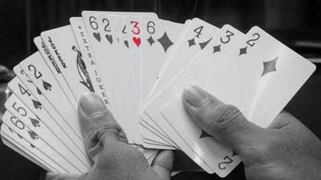 A selection of playing cards, with the three of hearts highlighted in colour. Adaptation of 'gaming cards in hands' by Midhun Joy from Pexels (free to use licence).