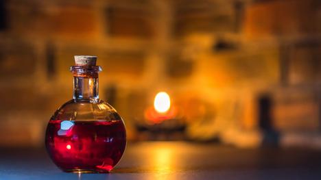 A mystical potion bottle glows warmly in candlelight against a rustic brick background.